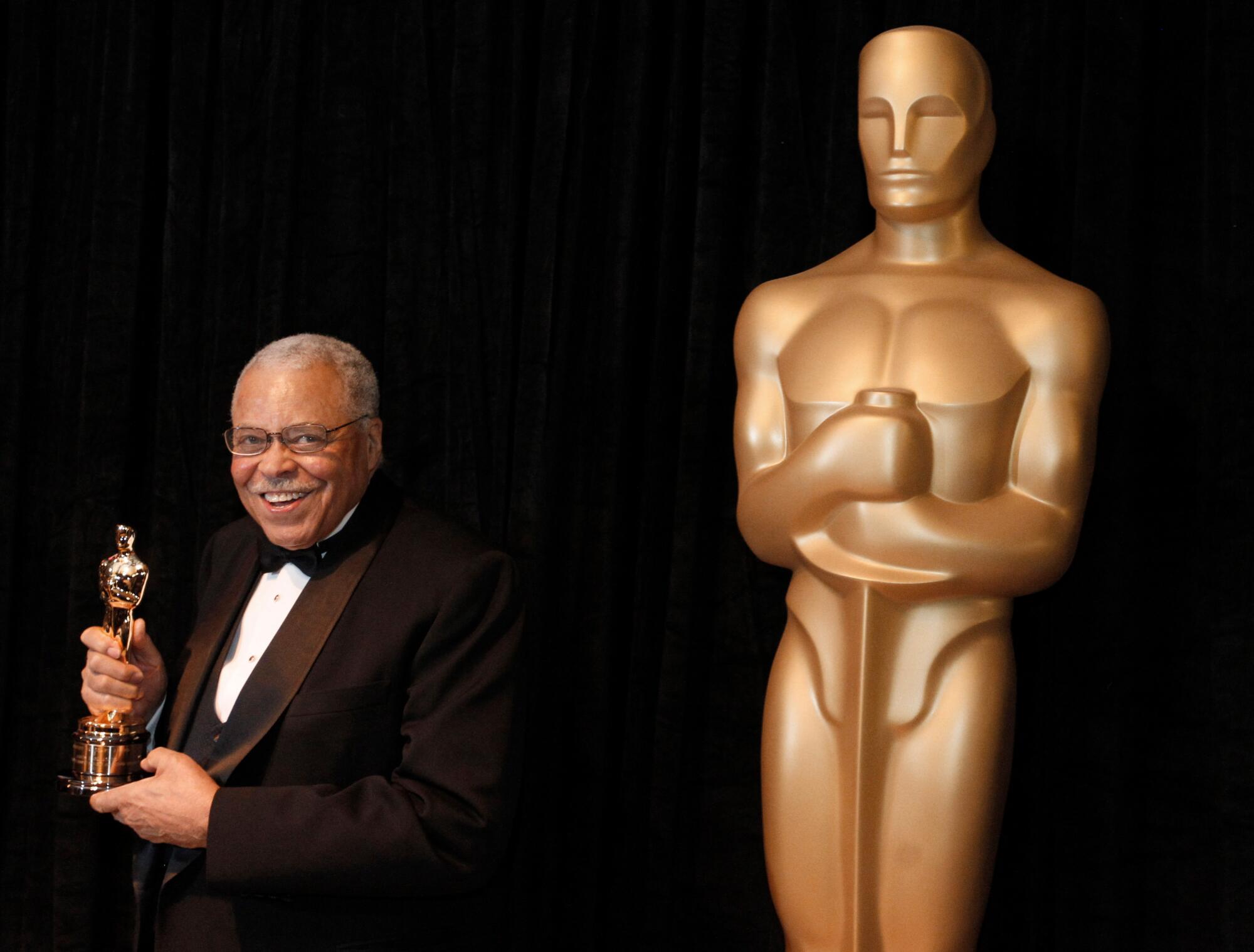 James Earl Jones sostiene una estatuilla del Oscar y se encuentra junto a una estatua de gran tamaño de un Premio de la Academia.