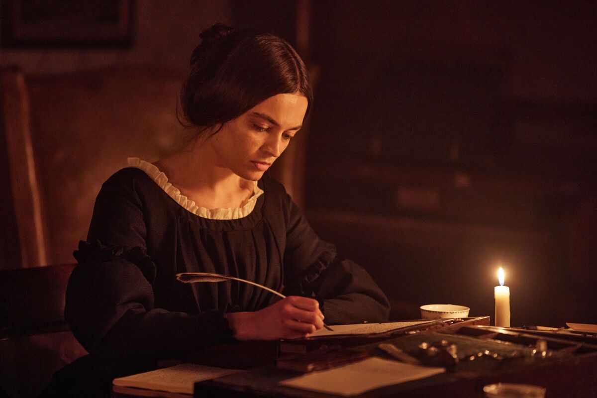 A woman in 19th century garb writes by candlelight.