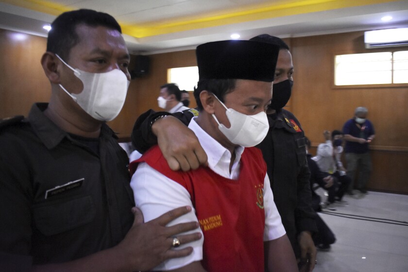 FILE - Herry Wirawan, center, the principal of a girls Islamic boarding school accused of raping his students, is escorted by security officers upon arrival for his sentencing hearing at a district court in Bandung, West java, Indonesia, on Feb. 15, 2022. An Indonesian high court granted an appeal from prosecutors and sentenced Wirawan to death for raping at least 13 students over five years and impregnating some of them. (AP Photo/Rafi Fadh, File)