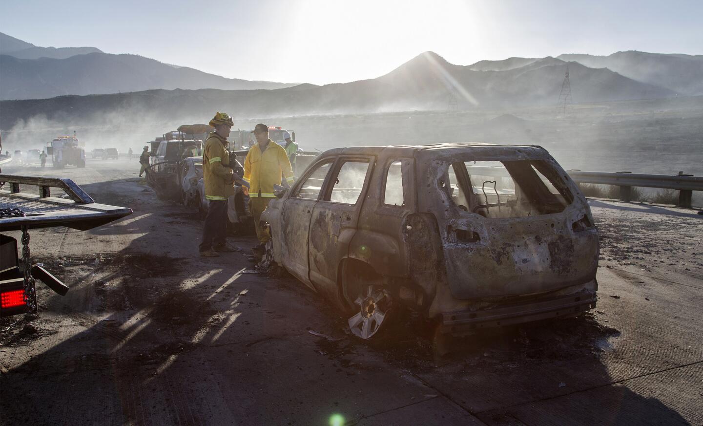 Firefighters stand amid the smoking wreckage of cars July 17, 2015, on Interstate 15 near Phelan, Calif. Dozens of people were forced to abandon their cars.