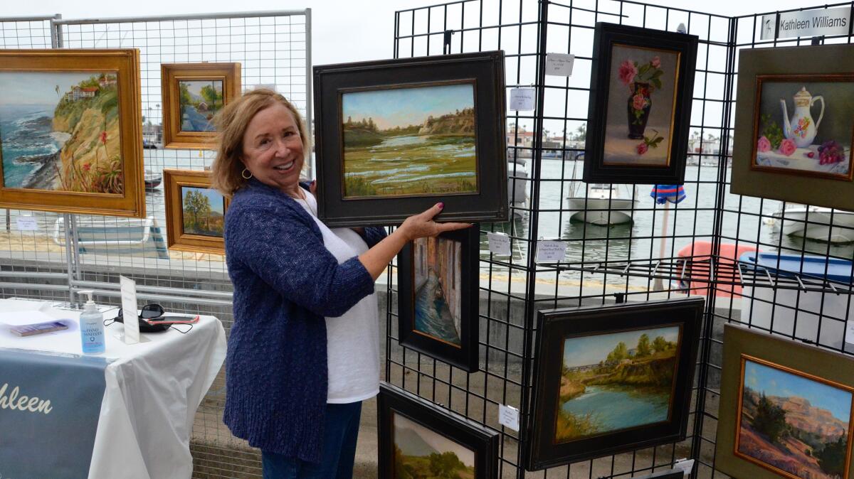 Plein-air painter Kathleen Williams holds her "Down On The Back Bay" painting during the Balboa Island ArtWalk on Sunday.
