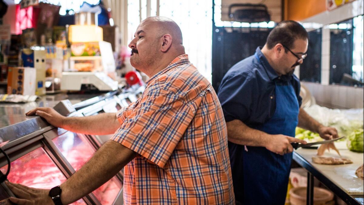 Isaac Gonzalez tends to a customer while his brother Juan Gonzalez cuts chicken. The siblings share ownership of Carniceria Don Juan, which has two locations.