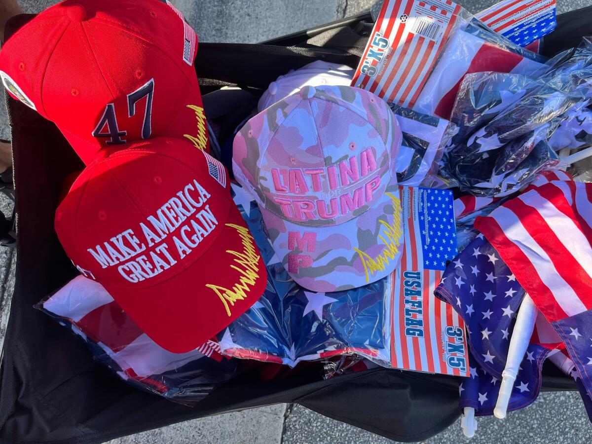 A range of merchandise including flags, red MAGA hats and pink camouflage "Latina for Trump" hat