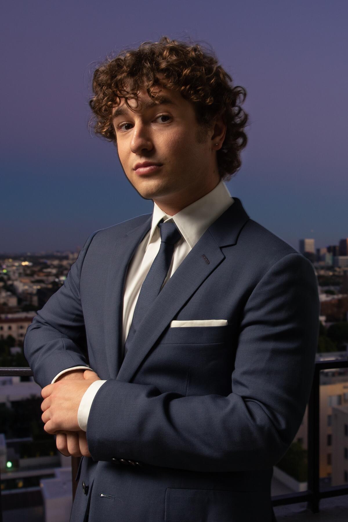 Gabriel LaBelle poses for a portrait wearing a blue suit and standing against a dusky sky.