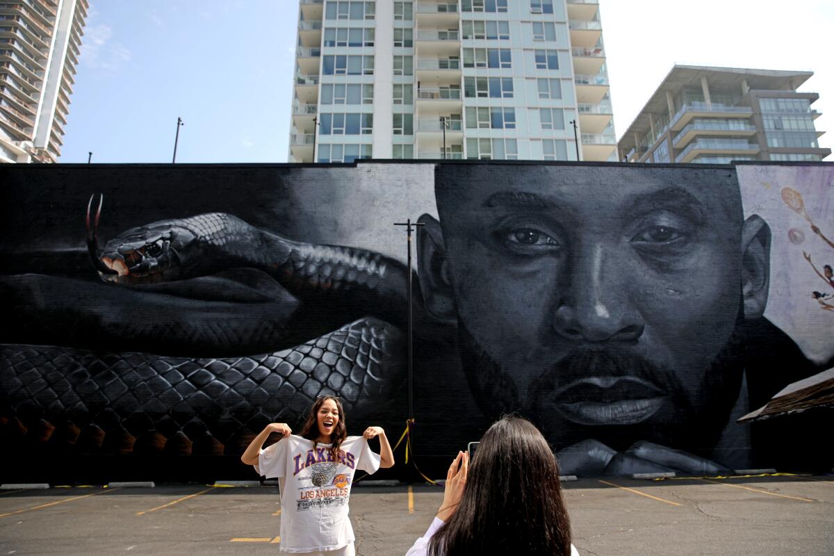 A woman takes another woman's photo in front of a mural of Kobe Bryant.