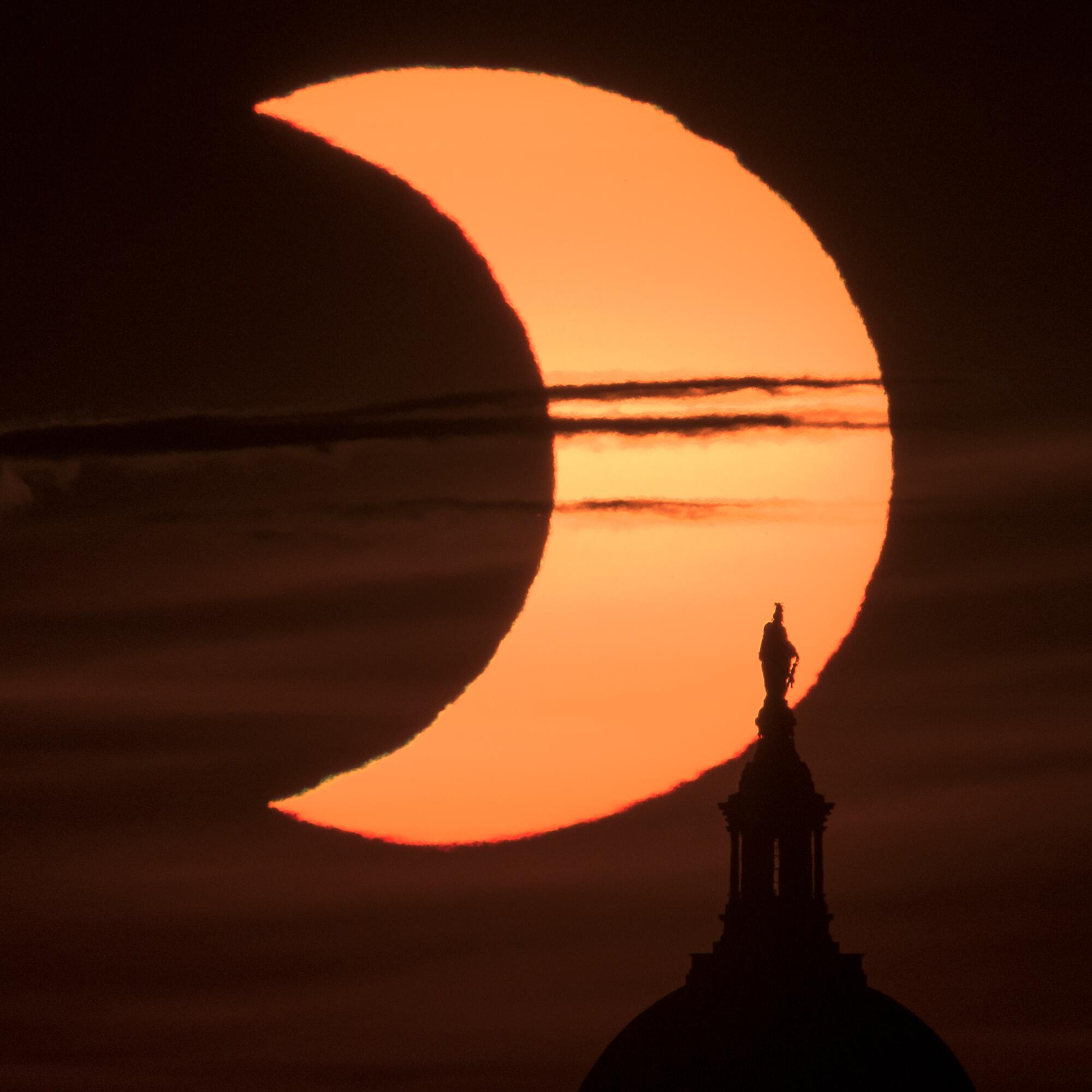 A partial solar eclipse is seen as the sun rises behind the Capitol Building in Arlington, Va.