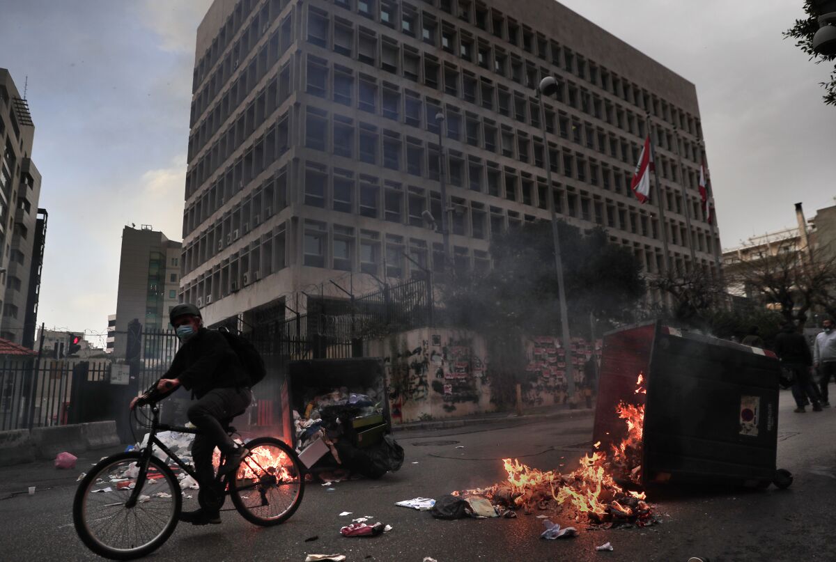 FILE - In this Monday, March 22, 2021, file photo, a man rides his bicycle past garbage containers set on fire by protesters blocking a main road in front the Lebanese Central Bank building, background, in Beirut, Lebanon. The World Bank said in a report released on Tuesday, June 1 that Lebanon's severe economic and financial crisis is likely to rank as one of the worst the world has seen in more than 150 years. (AP Photo/Hussein Malla, File)