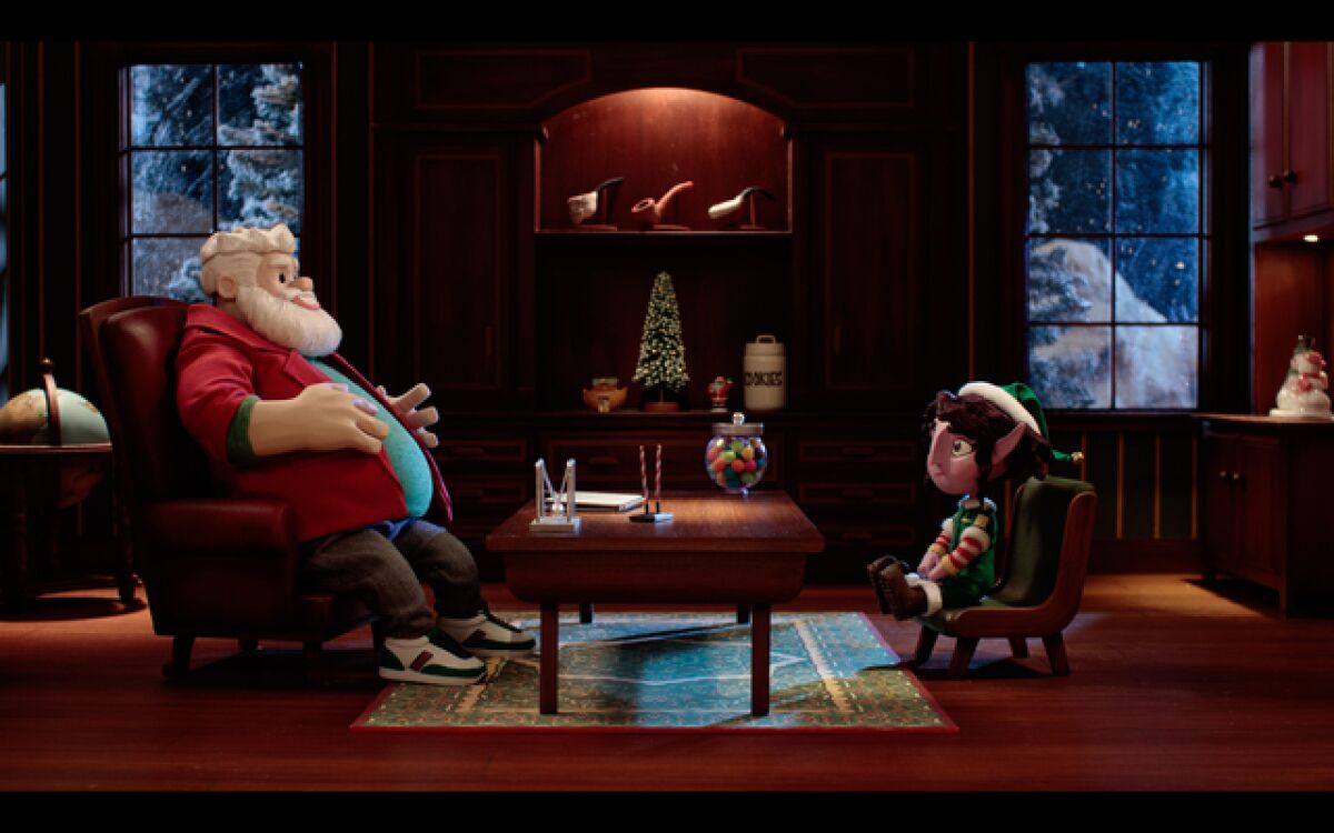An animated Santa and female elf sit across from each other in an office
