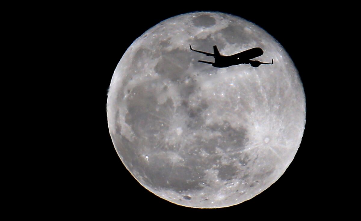 A jetliner making an approach to LAX is silhouetted as it flies in front of the moon. 