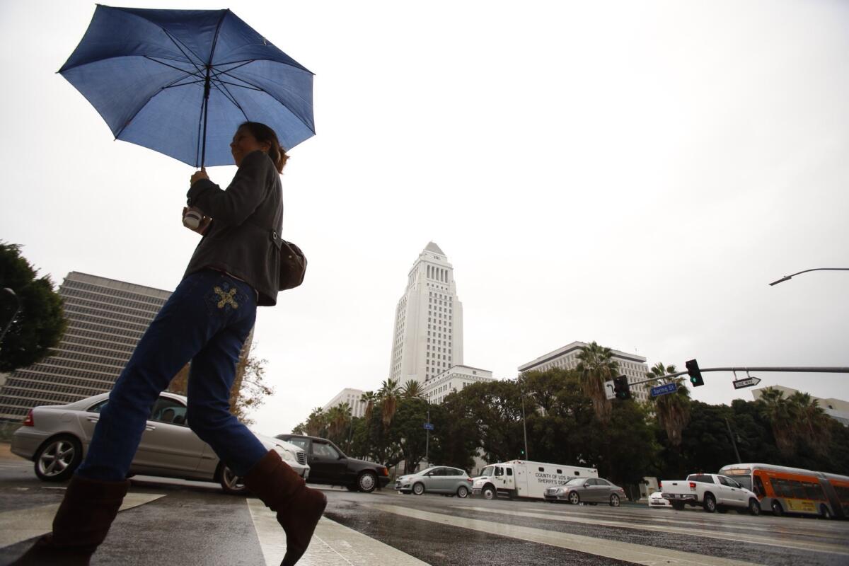 A pedestrian crosses the rain-slicked street under gray skies in downtown Los Angeles in December.
