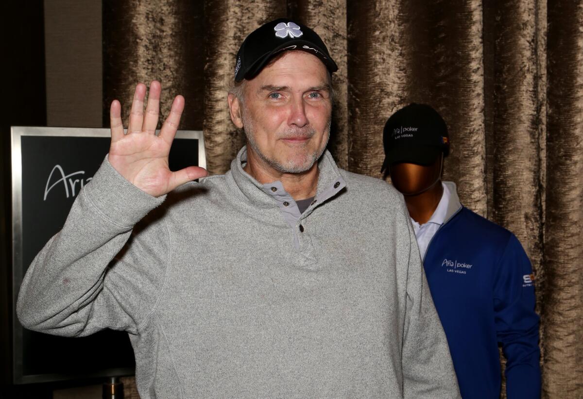 A man in a hat and sweatshirt waves at the camera.