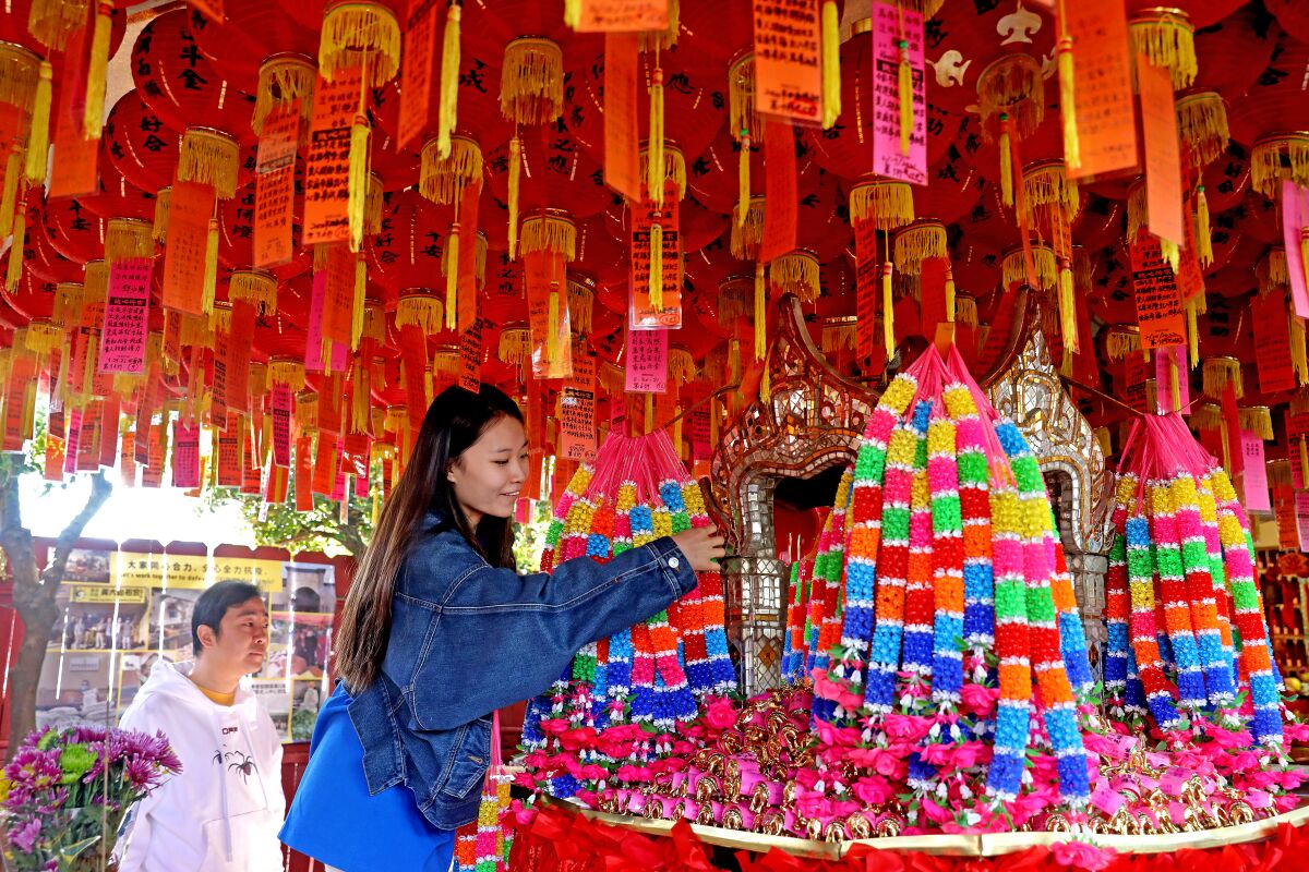 Jingjing Guo, right, with partner Chenggang Zhu, make an offering at a four-faced Buddha shrine