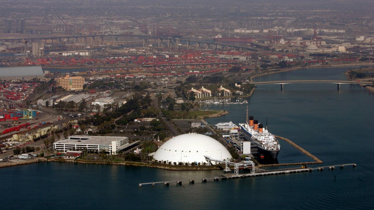 An aerial view of the Queen Mary and the dome that was the former home of the Spruce Goose, with cargo ports in the background, at the Port of Long Beach.