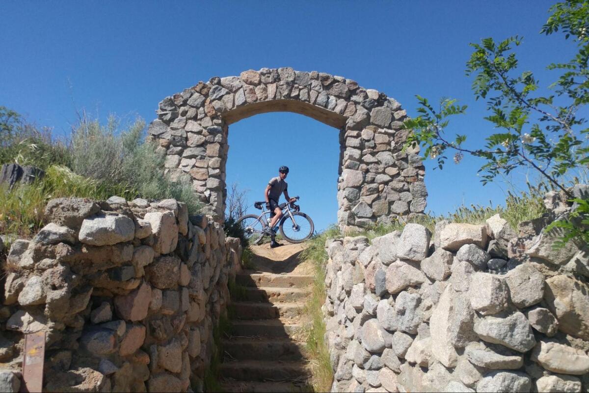 A cyclist poses under an old stone arch at the top of a short flight of steps.