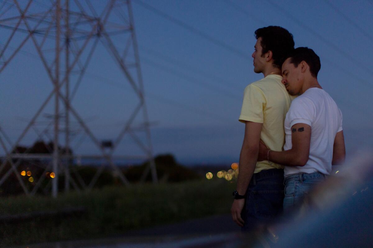 A boy embraces another boy from behind at dusk