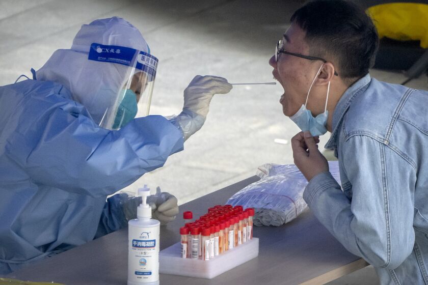FILE - A worker in a protective suit swabs a man's throat for a COVID-19 test at a testing site in an office complex in Beijing, Friday, April 29, 2022. The World Health Organization on Thursday, May 5, 2022 is estimating that nearly 15 million people were killed either by the coronavirus or by its impact on overwhelmed health systems in the past two years, more than double the official death toll of 6 million. (AP Photo/Mark Schiefelbein, File)
