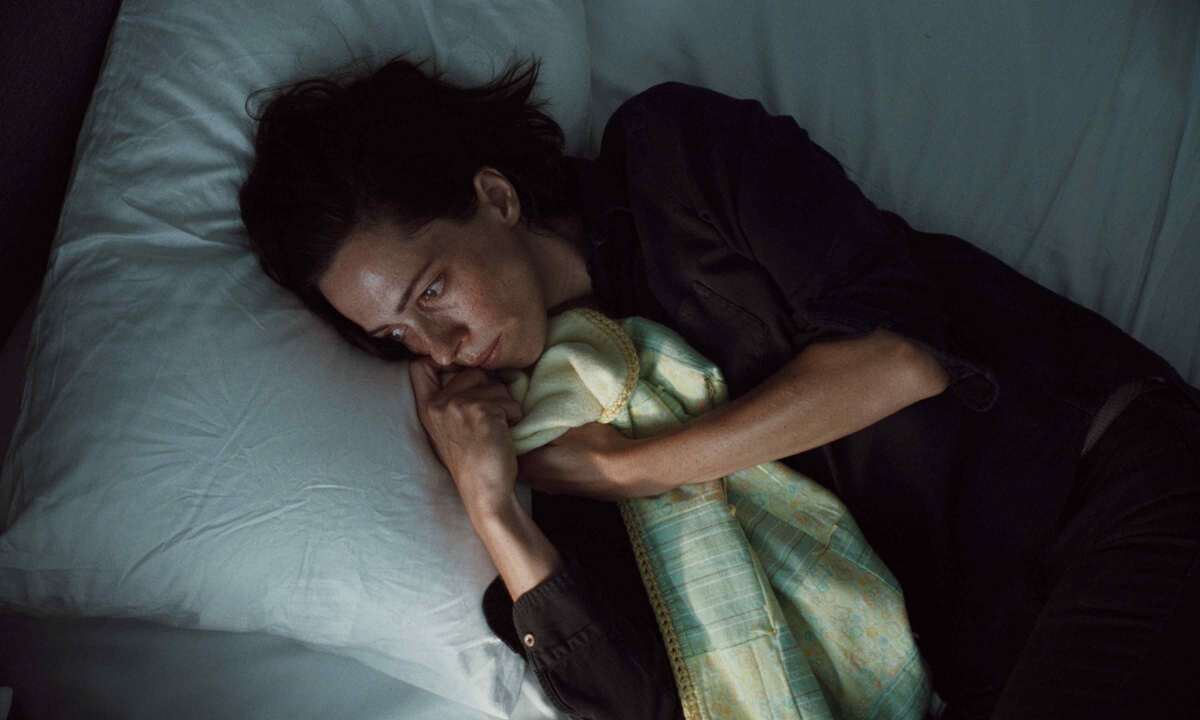 A woman on a bed clutches a blanket.