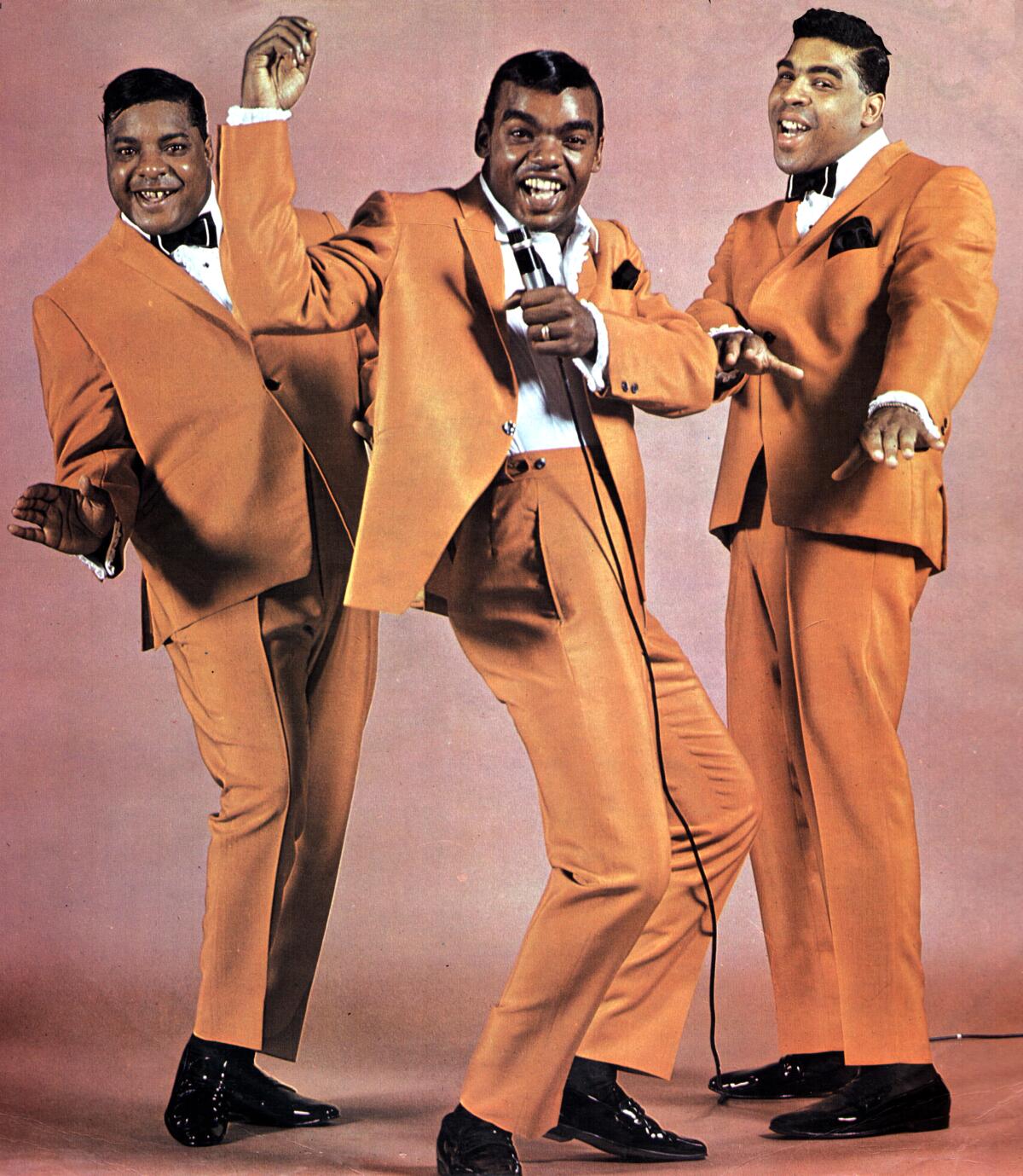 Three R&B singers in matching orange tuxedos