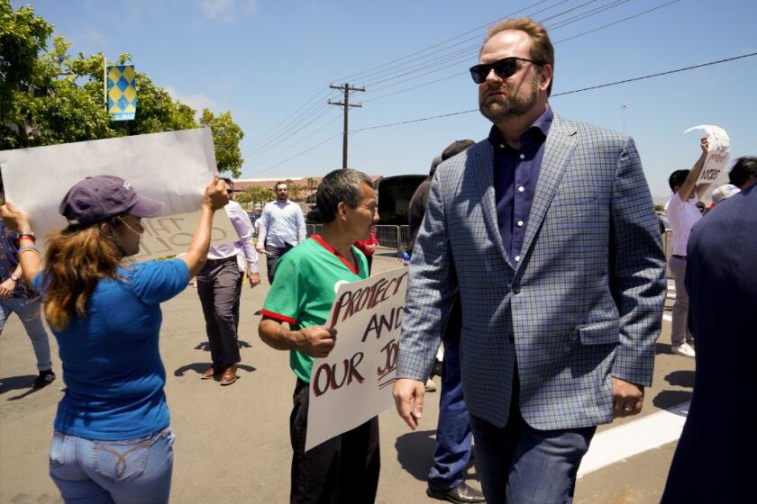 On opening day at Del Mar on July 17, 2019, Doug O'Neill walks by a protest showing support for workers who work with the race horses.