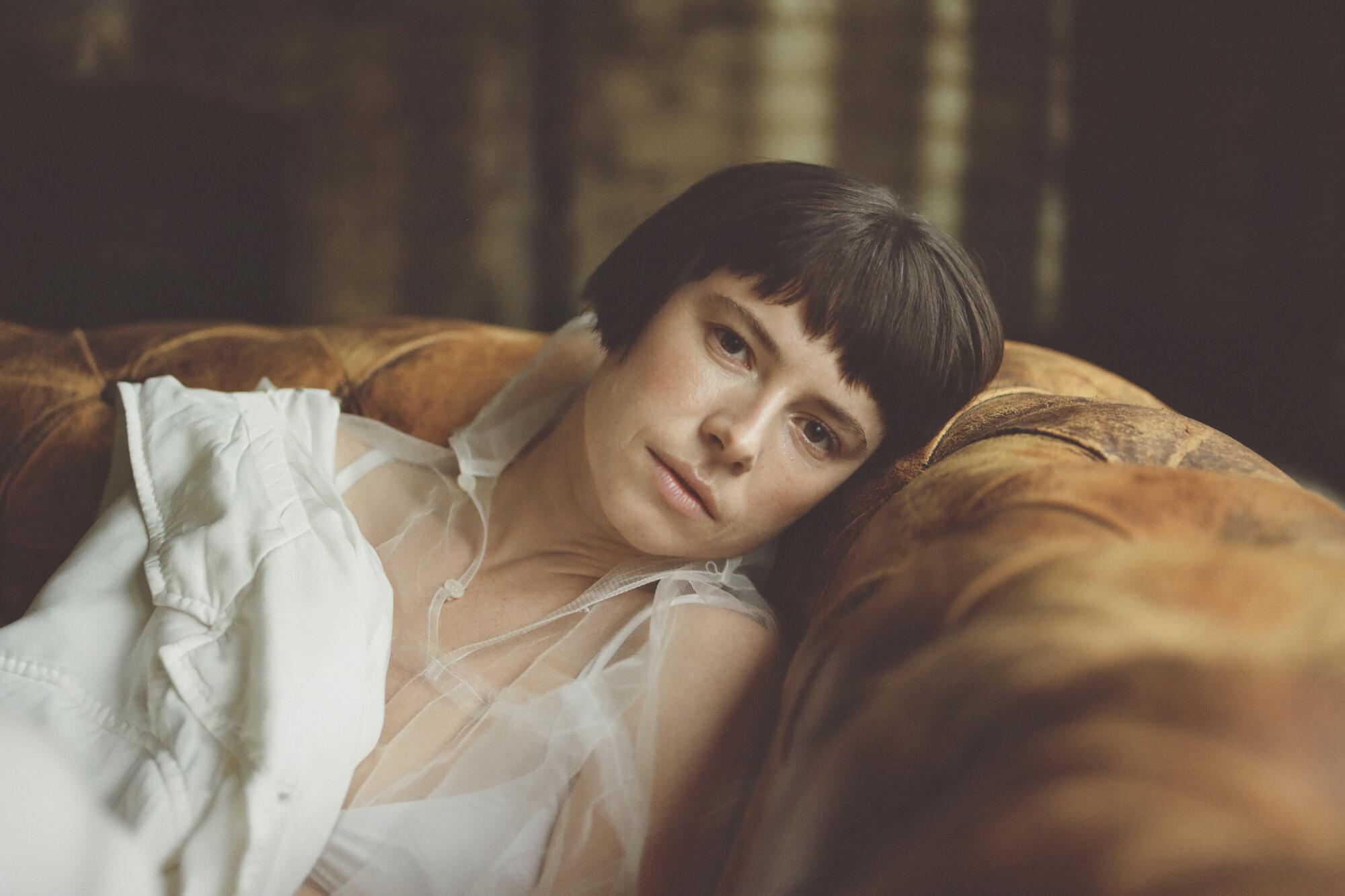 A portrait of Jessie Buckley, head leaning against the back of a couch.