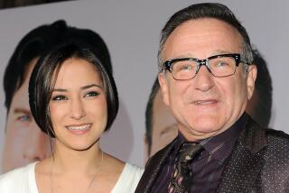 A young woman with short black hair in a white shirt smiling next to Robin Williams in glasses and a dark suit