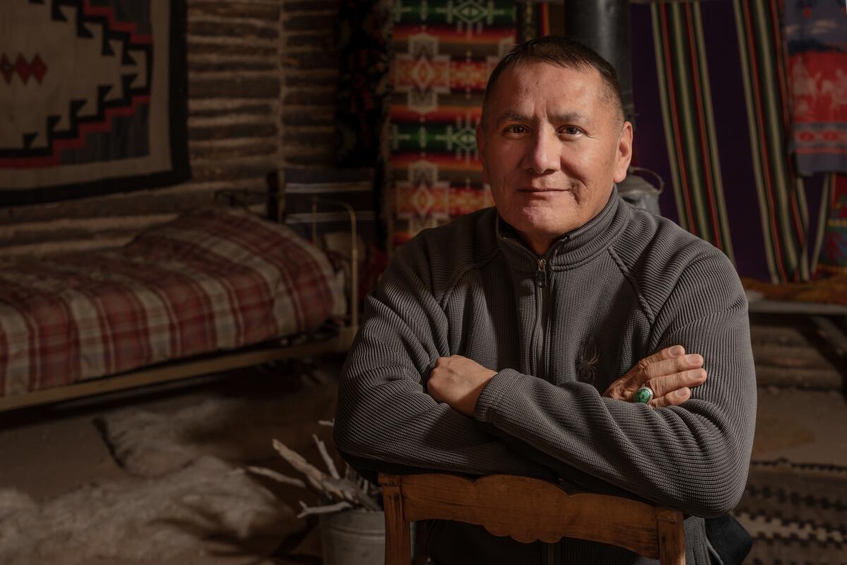 A man in a gray sweatshirt with his arms crossed in a Navajo hogan.