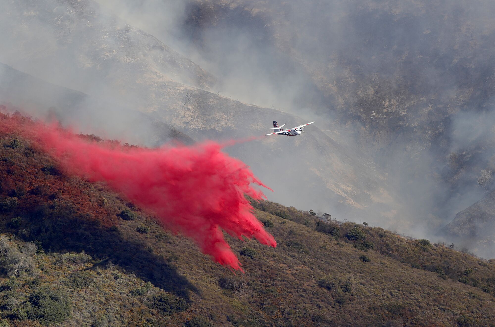 Bright red fire retardant dropped by an airplane above a smoky hillside