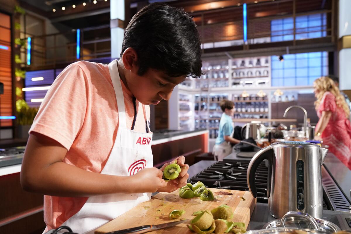 A child chef slices kiwi in an industrial kitchen.