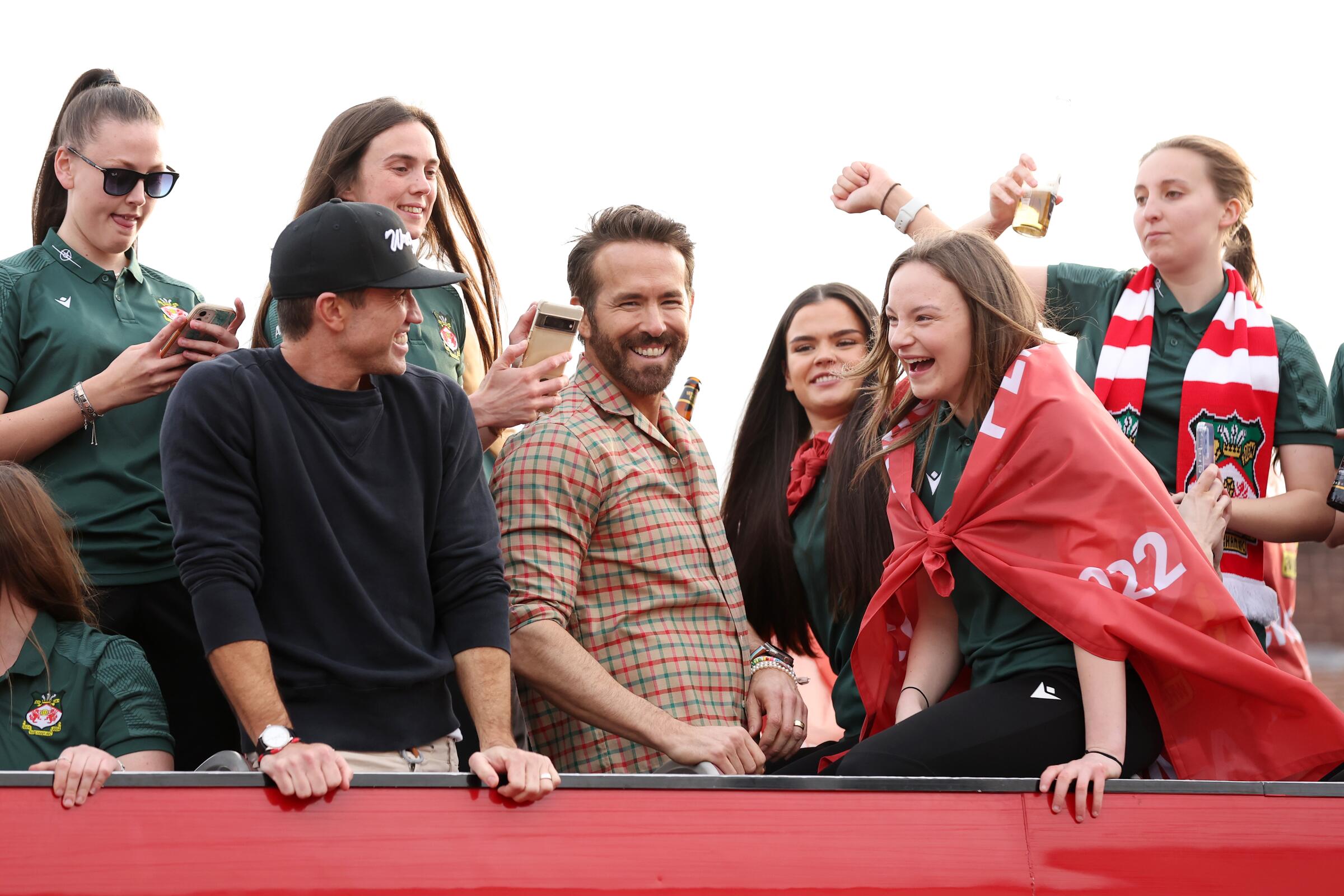 Ryan Reynolds, center, and Rob McElhenney ride on a parade bus with players.