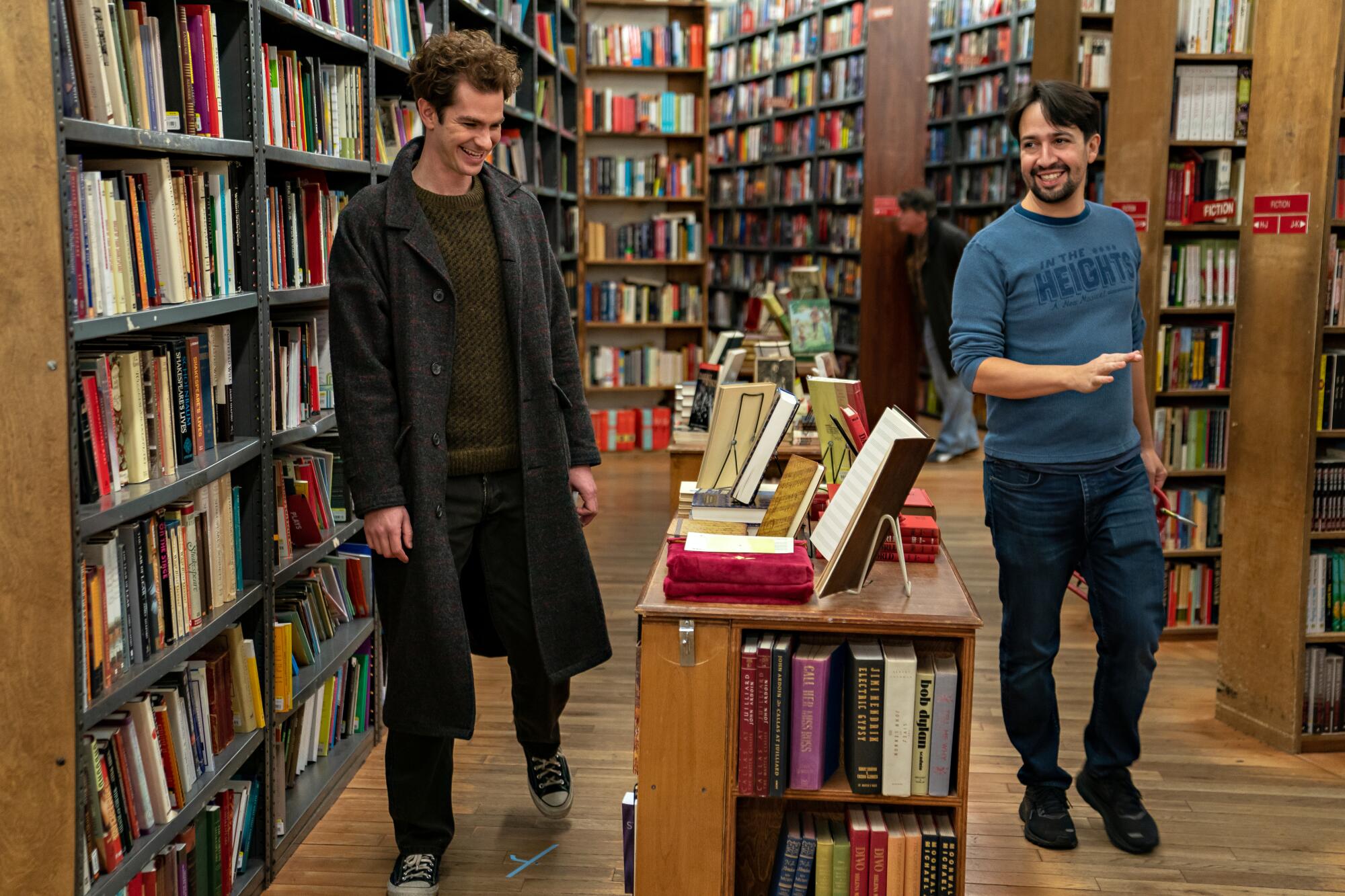Andrew Garfield and Lin-Manuel Miranda stand among bookshelves.