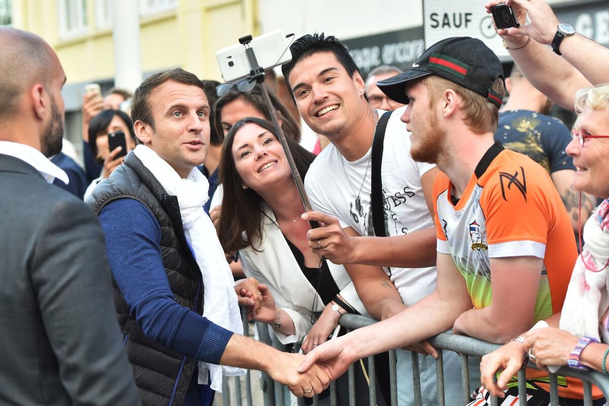 French President Emmanuel Macron, left, poses for a selfie as he arrives in Le Touquet, northern France, the city where he votes, on the eve of France's legislative elections.