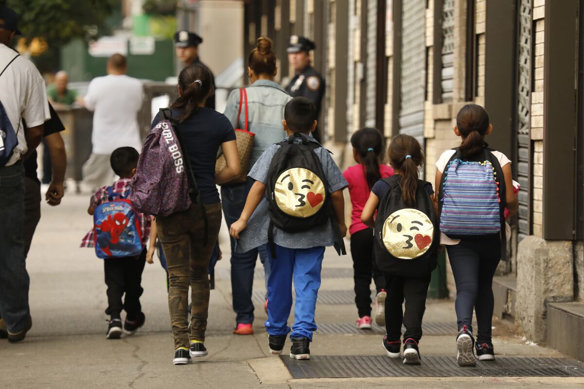 Children wearing backpacks walk together along a New York sidewalk.