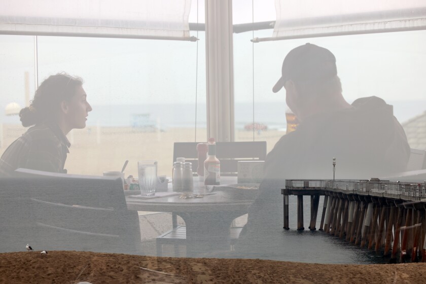 In a double exposure, Leah Barnum, left, and D.A. Jones eat at Hennessey's Tavern and the pier is seen.