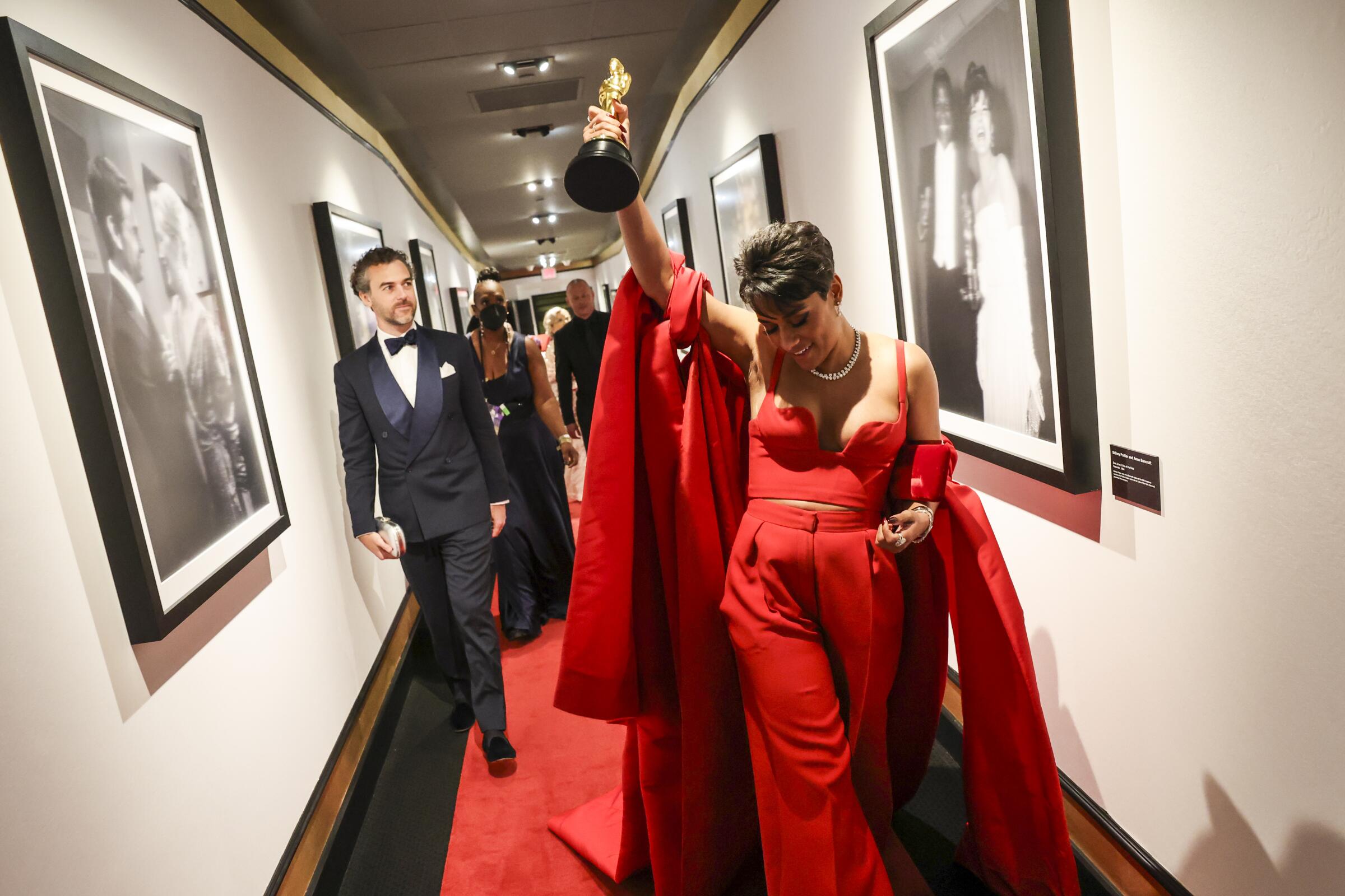 Ariana DeBose walks backstage at the 2022 Oscars, hoisting her statuette.