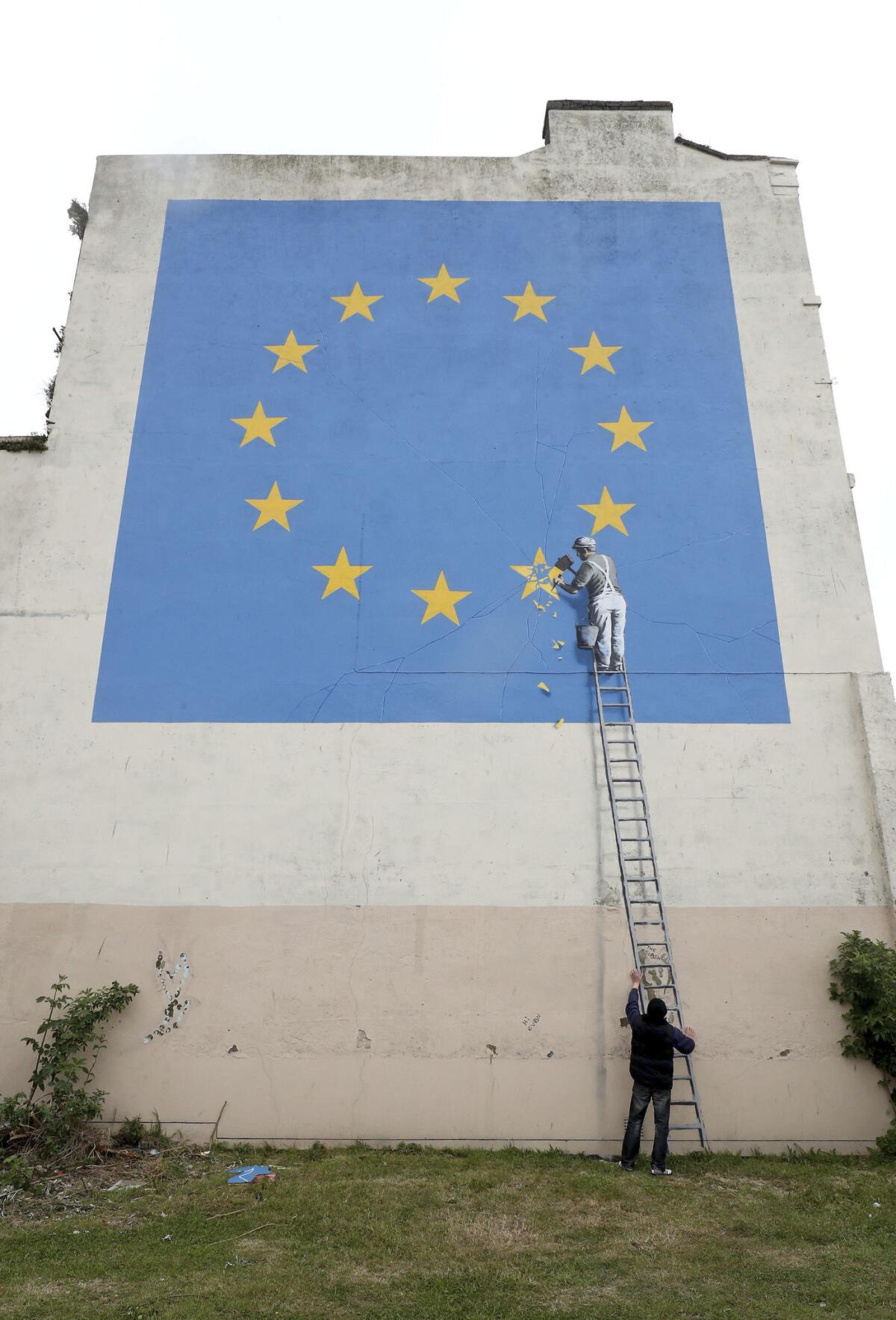 Un hombre, abajo, posa para una foto al pie de un mural del artista callejero Banksy en Dover, Inglaterra, el lunes 8 de mayo del 2017. El mural muestra a un trabajador borrando con un cincel una de las 12 estrellas de la bandera de la UE, alusivo a la decisión de Gran Bretaña de salirse de la Unión Europea. (Gareth Fuller/via AP)