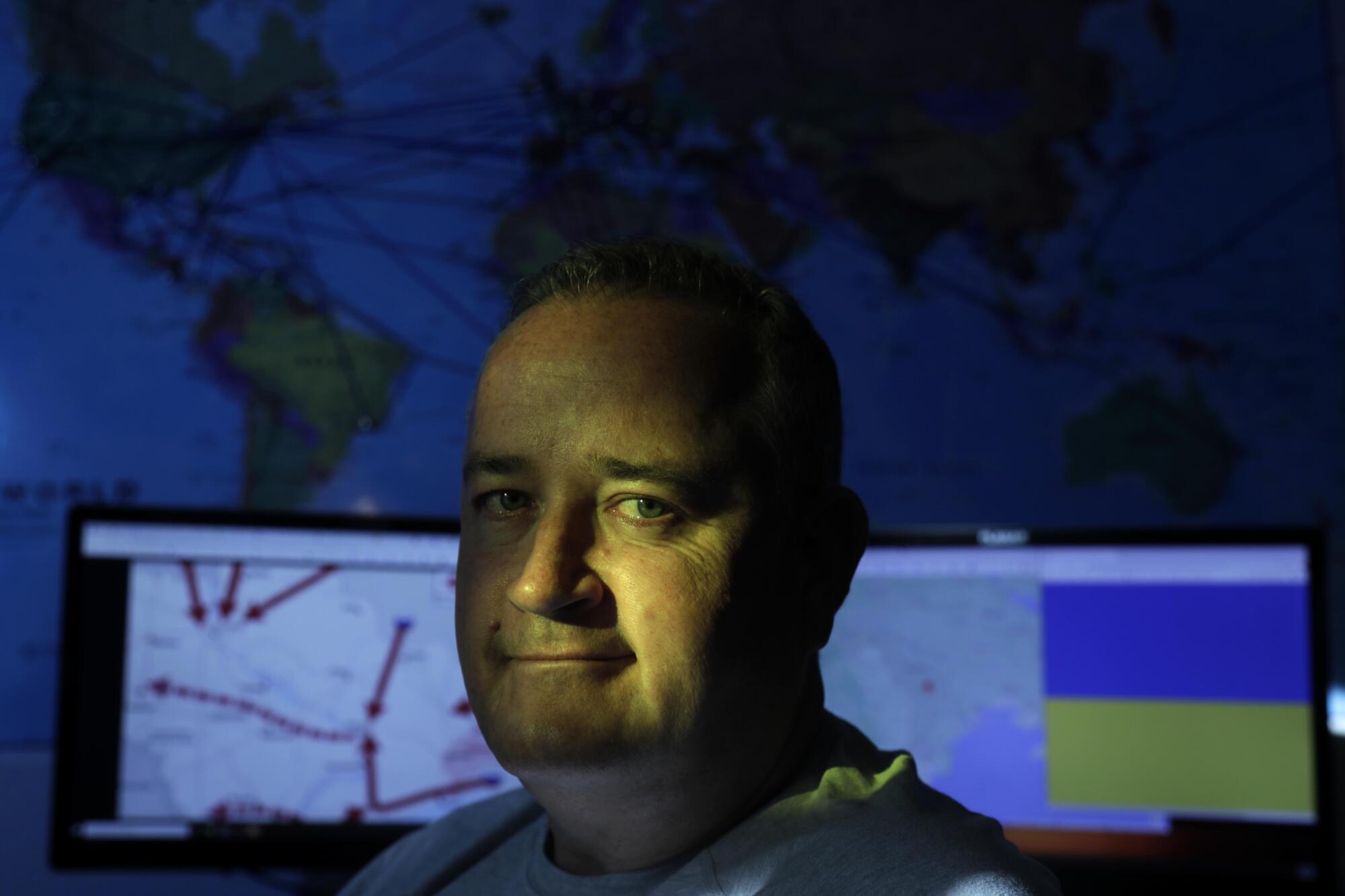 A portrait of a man against a background of computer screens and a large map