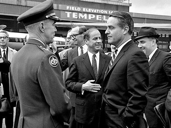 Shriver, as director of the Peace Corps, is welcomed at Tempelhof Airport in Berlin, on April 25, 1964. Talking with Shriver is Maj. Gen. James H. Polk, the U.S. commandant in Berlin. In the center is John A. Calhoun, the top U.S. State Department official in Berlin. See full story