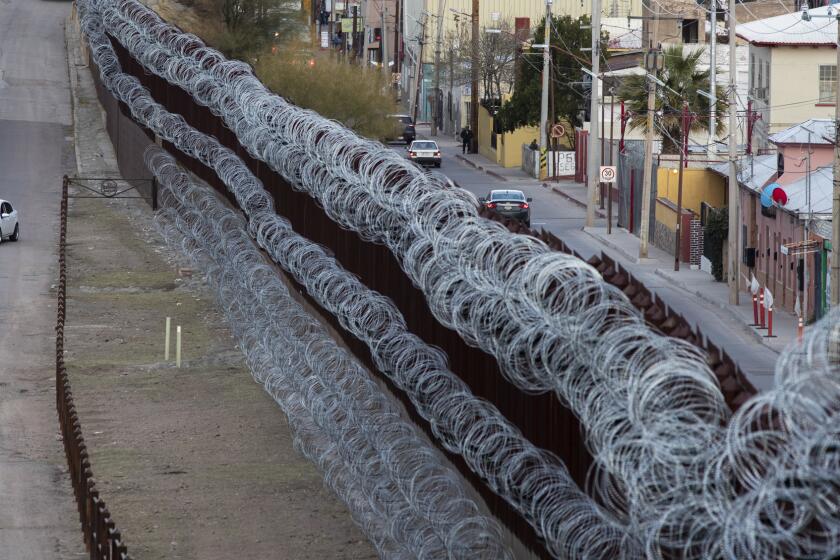 NOGALES, ARIZ. -- MONDAY, MARCH 4, 2019: A vehicle, left, makes a turn on International Street in Nogales, Ariz. across border fence from Nogales, Sonora, Mexico, right. City officials in Nogales, Ariz. want the federal government to remove concertina wire installed on existing steel fence by U.S. Army troops earlier this year in Nogales, Ariz., on March 4, 2019. (Brian van der Brug / Los Angeles Times)