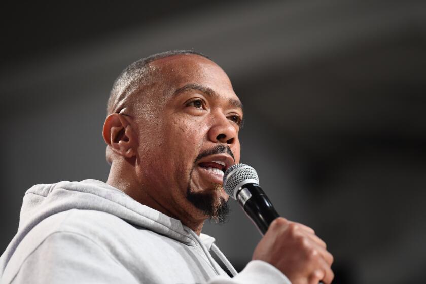 Timbaland talks as he holds a microphone to his mouth and his wearing a light gray hoodie