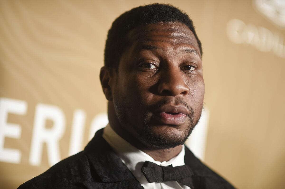 Jonathan Majors in a black suit and bowtie against a yellow background