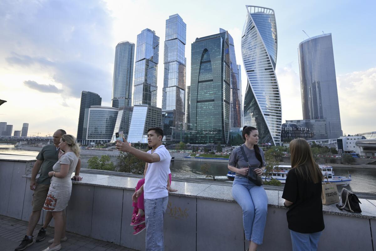 People pause on a walkway alongside the Moscow River opposite the "Moscow City" business district