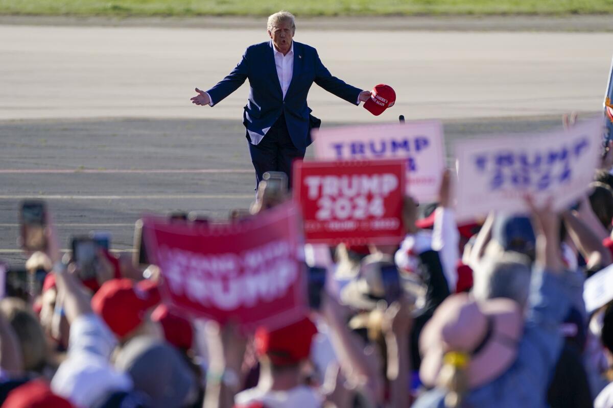 Former President Trump walking across the tarmac toward a crowd of supporters, many holding "Trump 2024" signs