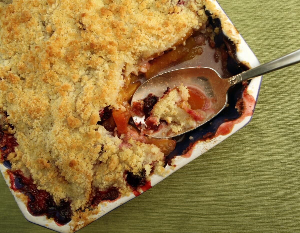 A pan of Peach and blackberry crisp, with a spoon resting in a scooped-out space