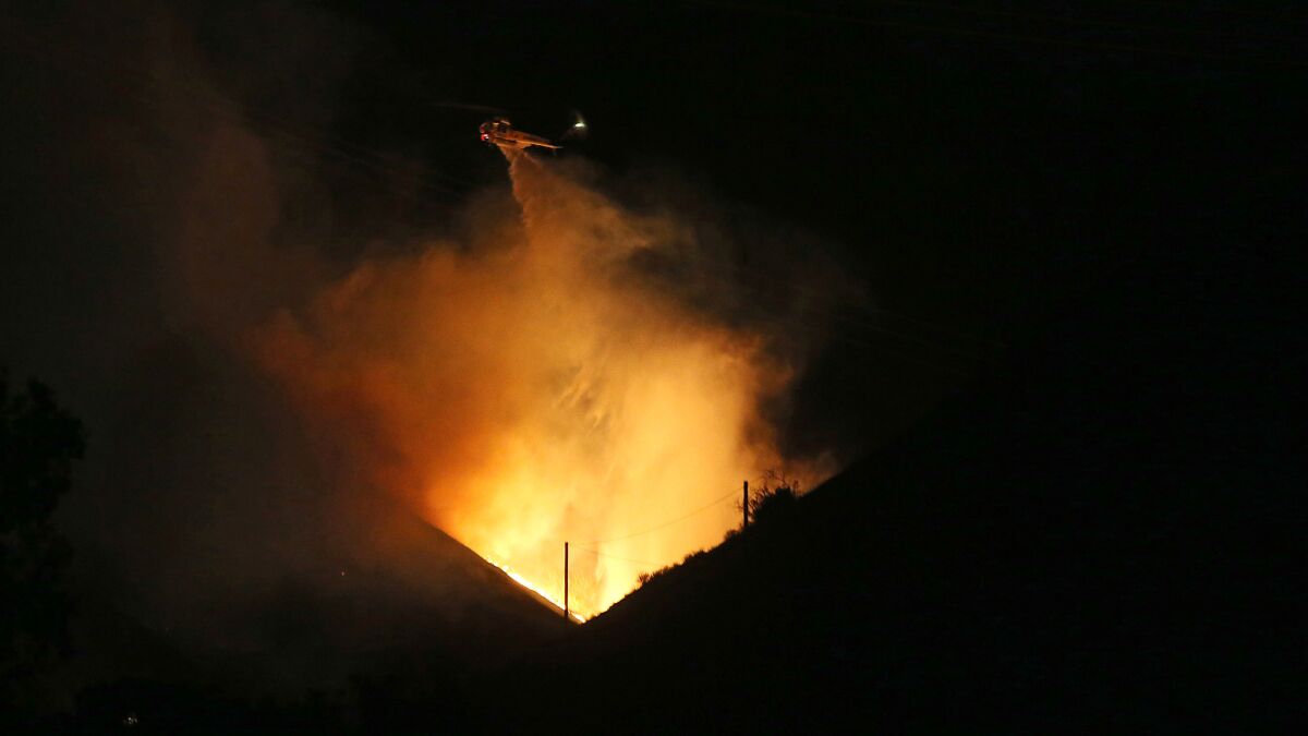 A firefighting helicopter makes a water drop on a wildfire in the hills of Porter Ranch on Oct 18.