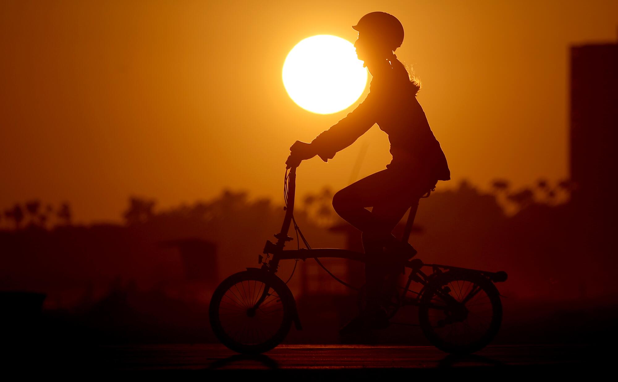 A bike rider is silhouetted by the sun and an orange sky.