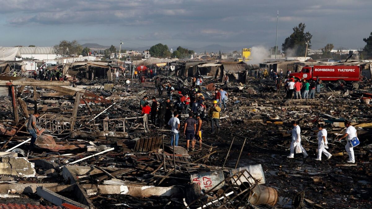 Firefighters and rescue workers walk through the scorched grounds of Mexico's best-known fireworks market after an explosion Tuesday.