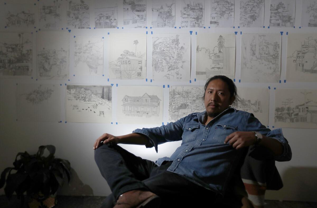 Artist Manuel Lopez framed by his drawings of hillside communities at his City Terrace studio.