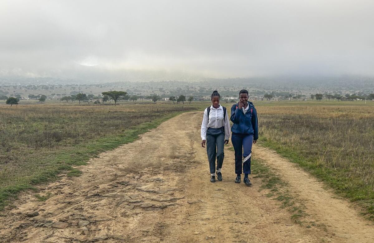 Two young people walk a dirt road surrounded by grass. 