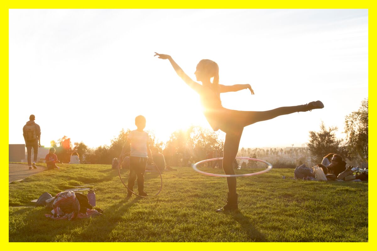 A woman hula hoops in a park at sunset