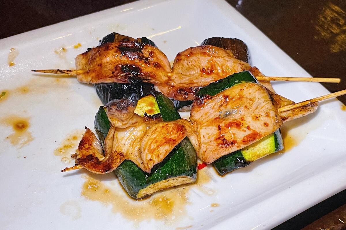 Two skewers of chicken-wrapped zucchini on a white plate